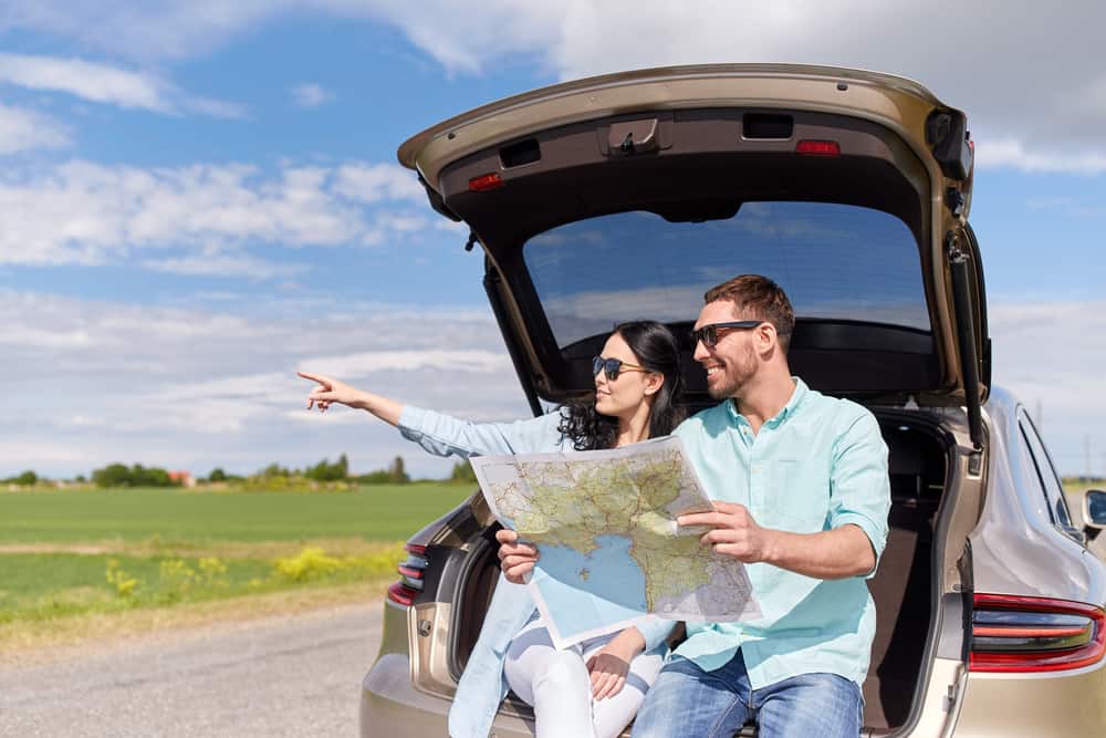 happy couple on the back of a car in road trip rental car insurance