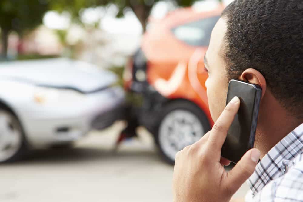 back view of a man talkin on cell phone with a car accident in the background