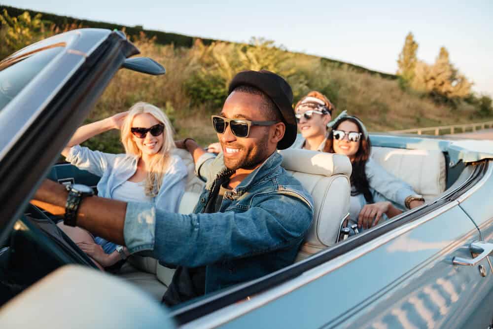 Group of cheerful young friends driving car and smiling in summer