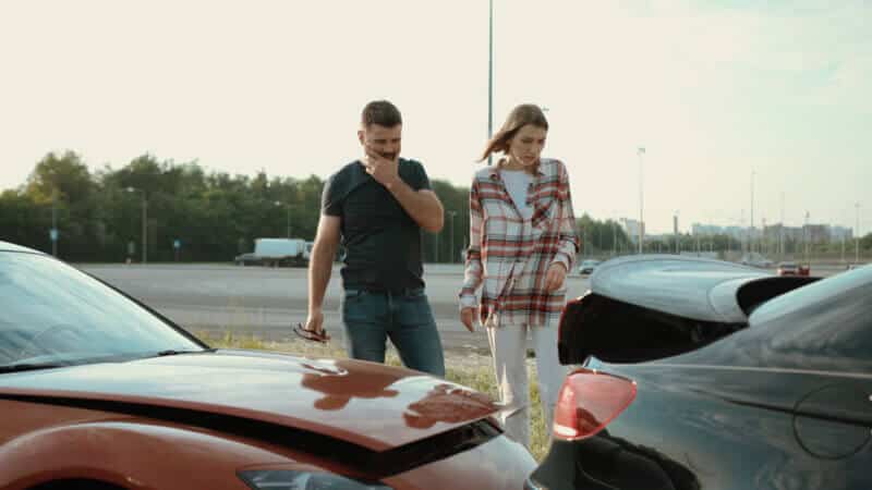 Upset man and woman looking on broken stuck cars after car accident.