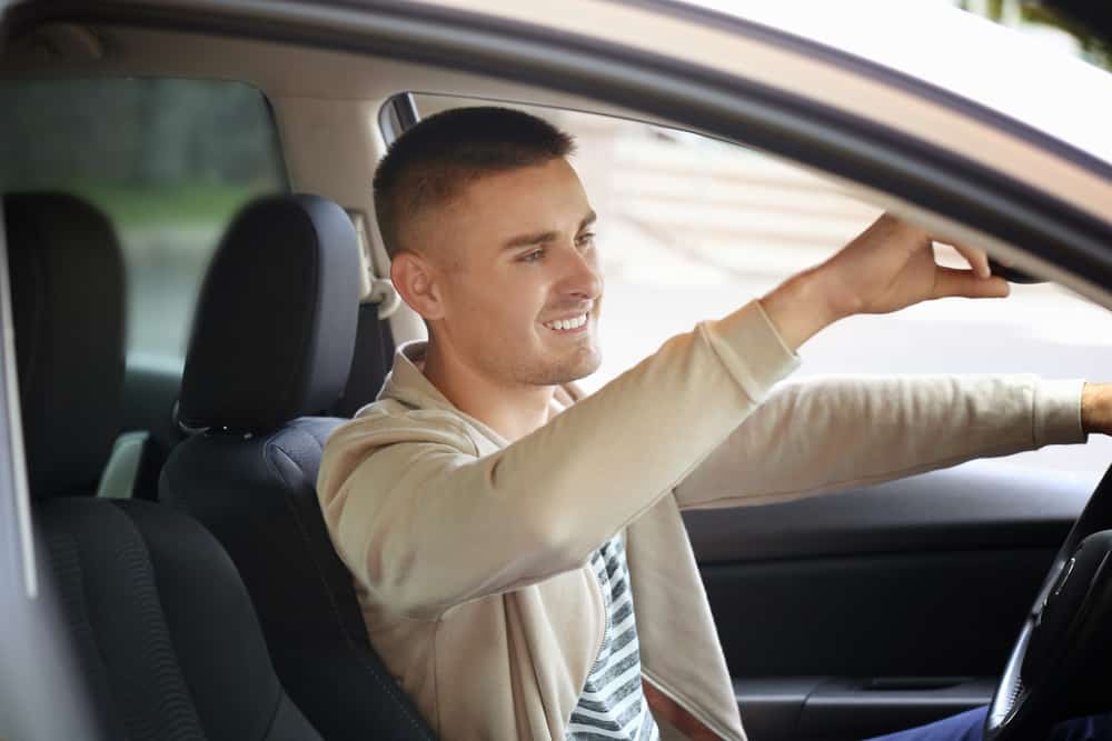 Happy young man adjusts his rearview mirror