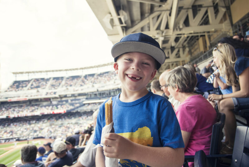 Snaggle-tooth kid happily enjoying a churro at the ball game