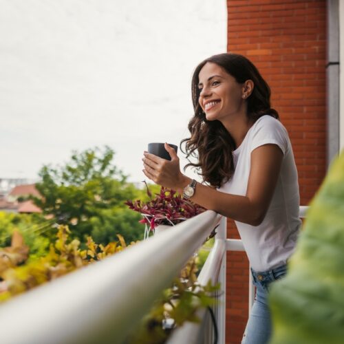 Young woman enjoys a cup of tea while standing on her apartment balcony