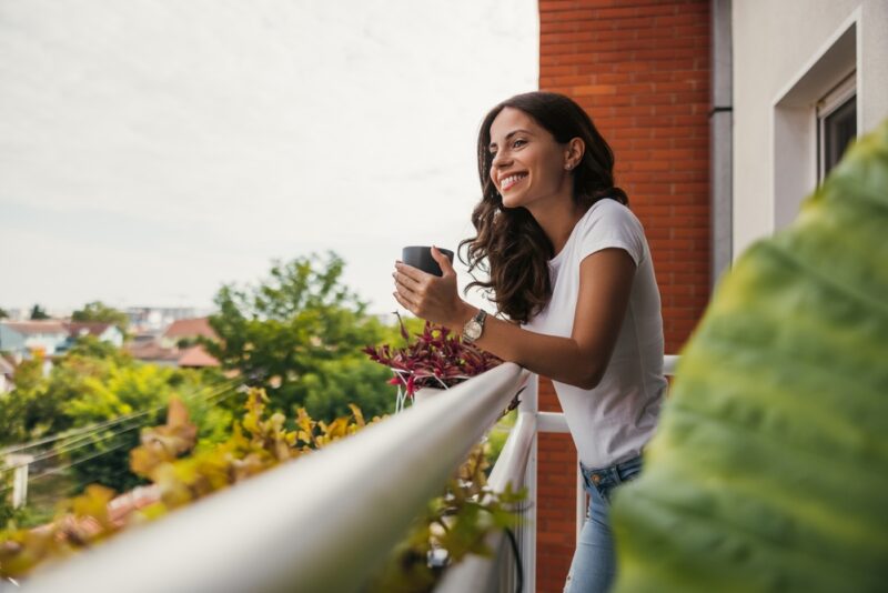 Young woman enjoys a cup of tea while standing on her apartment balcony