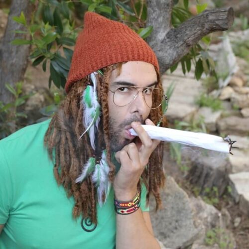 Man with dreads smoking a huge, rolled marijuana joint.