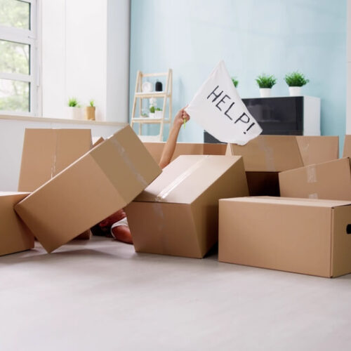 Pile of moving boxes on floor of new home with hand raised up through them holding a help sign - cheap homeowners insurance in Washington.