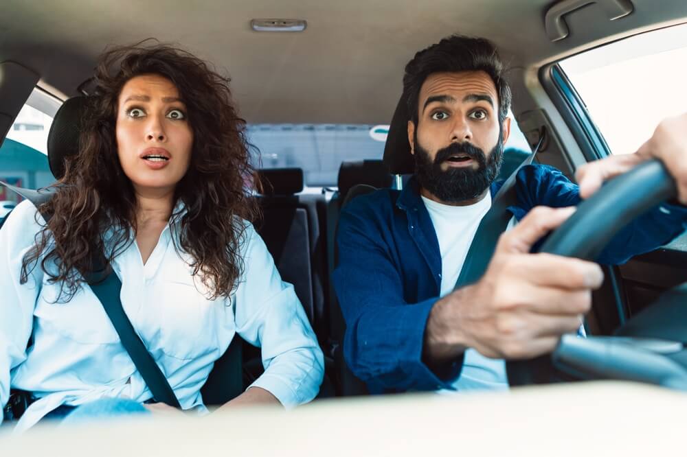 Couple in their car looking with shocked expressions out the front window.