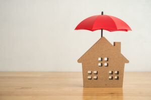 A cardboard house with a red umbrella over it.