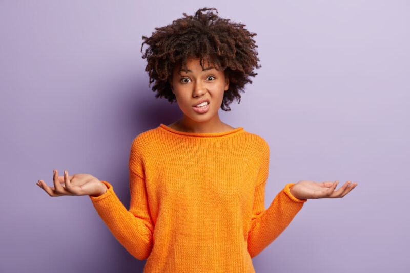 Confused woman in orange shirt with hands in air and puzzled expression on her face - cheap insurance in Washington State.