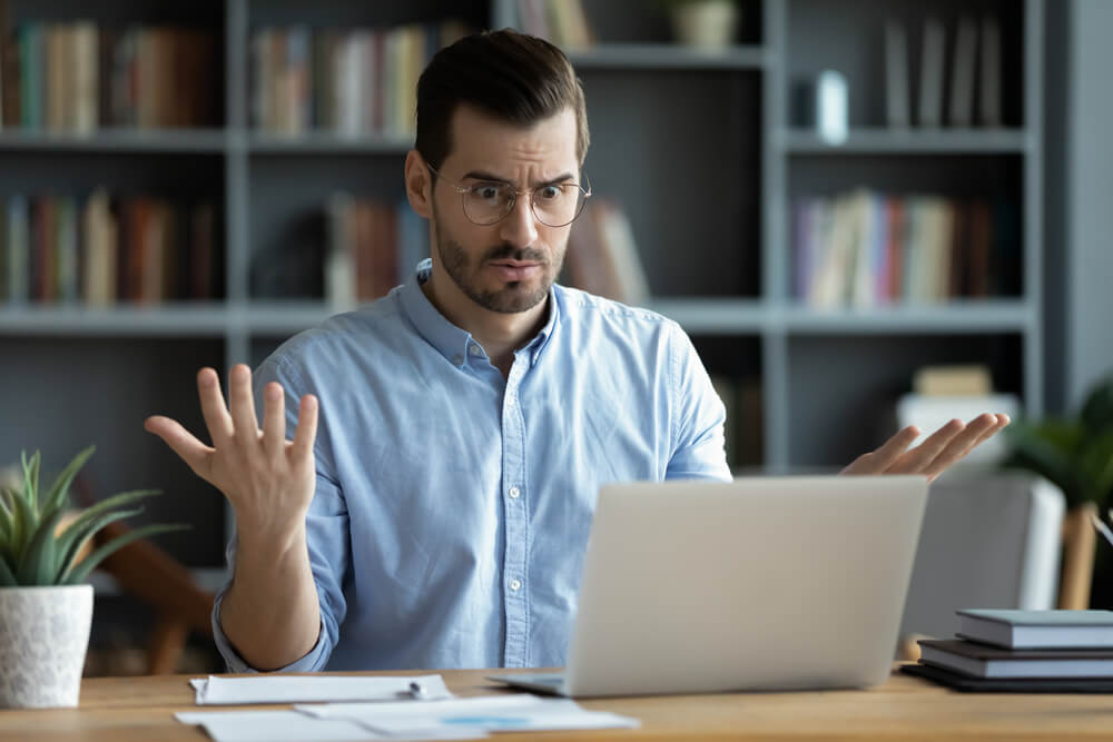 Man sits at laptop on desk with puzzled expression and hands in the air - cheap insurance in Washington state.